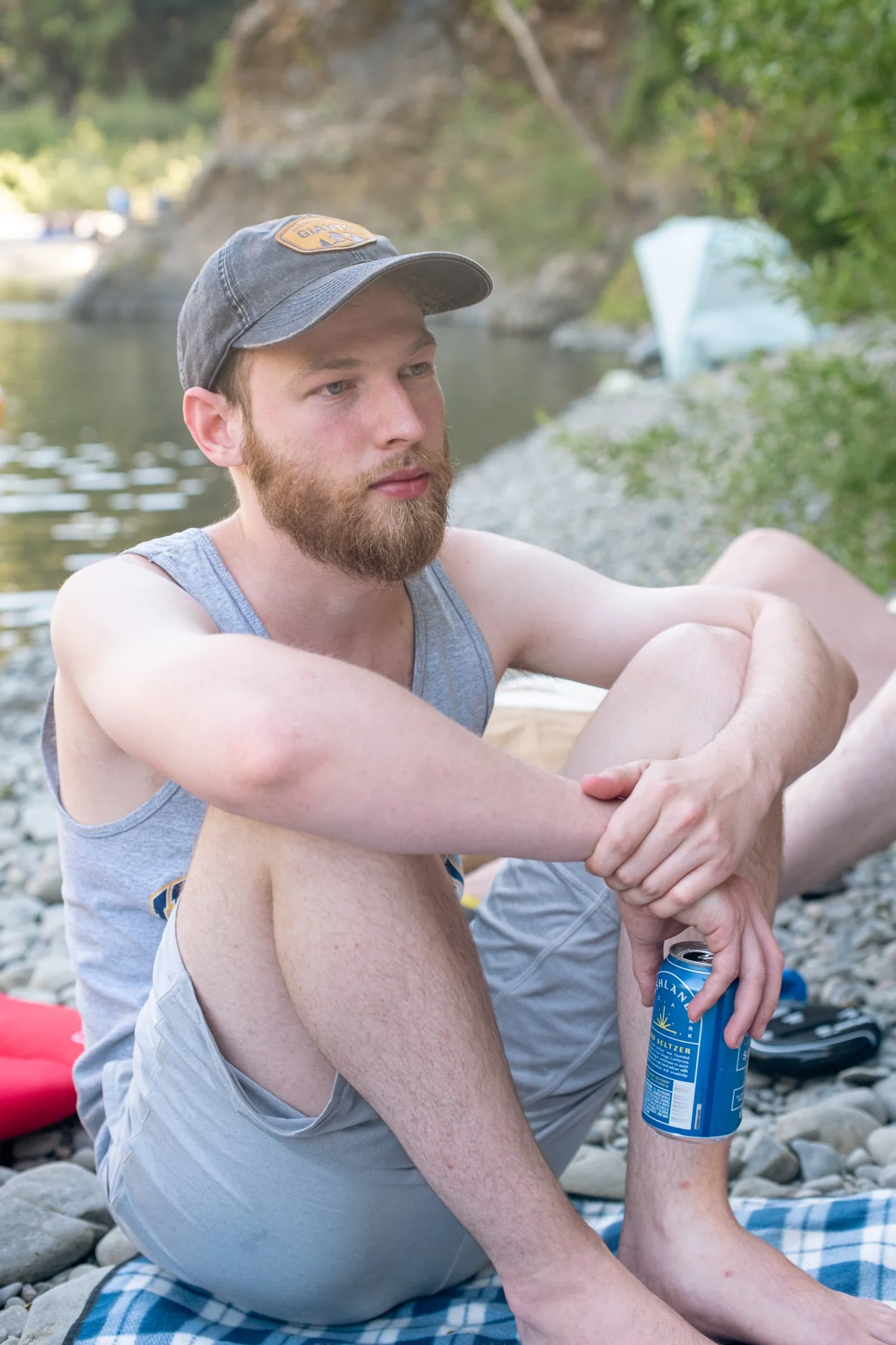 Bearded man in a cap sitting beside a creek.