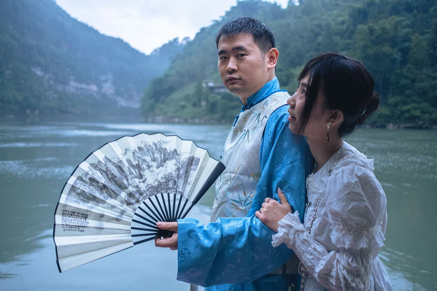 Couple beside a mountain lake, with the man holding an open folding fan.