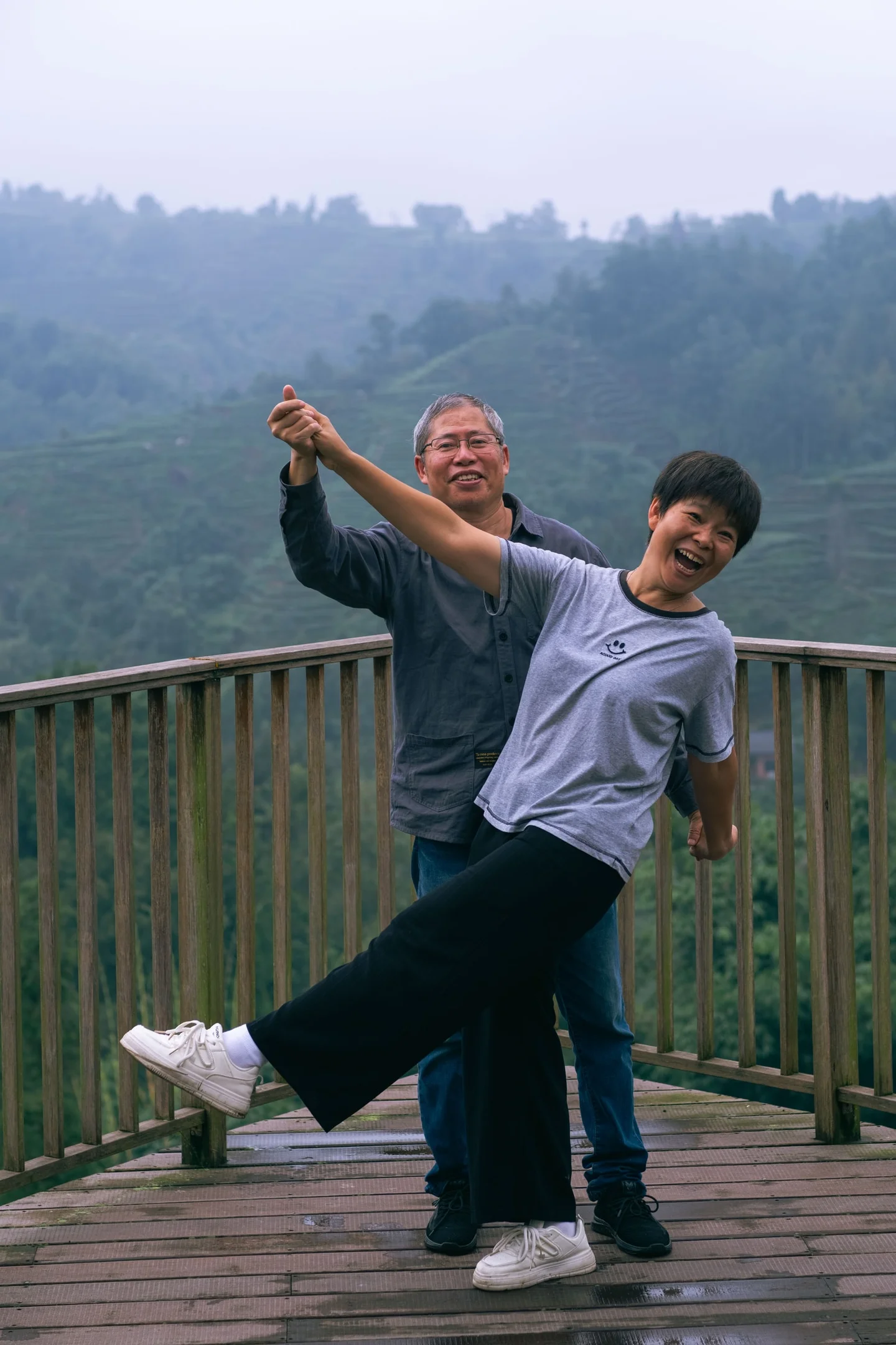 Two people laughing and dancing on a wooden lookout deck.
