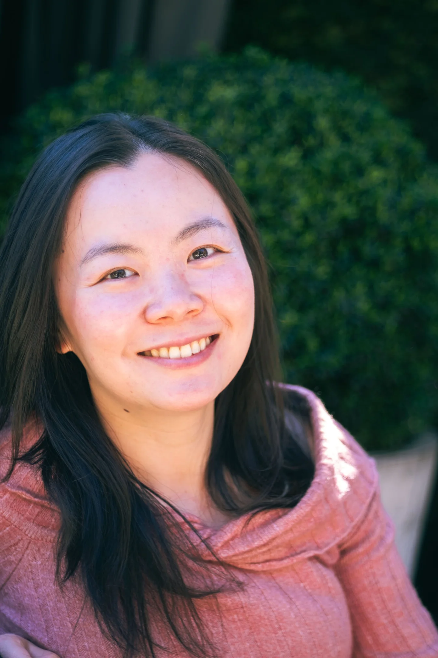 Smiling woman in a pink wrap against a leafy background.