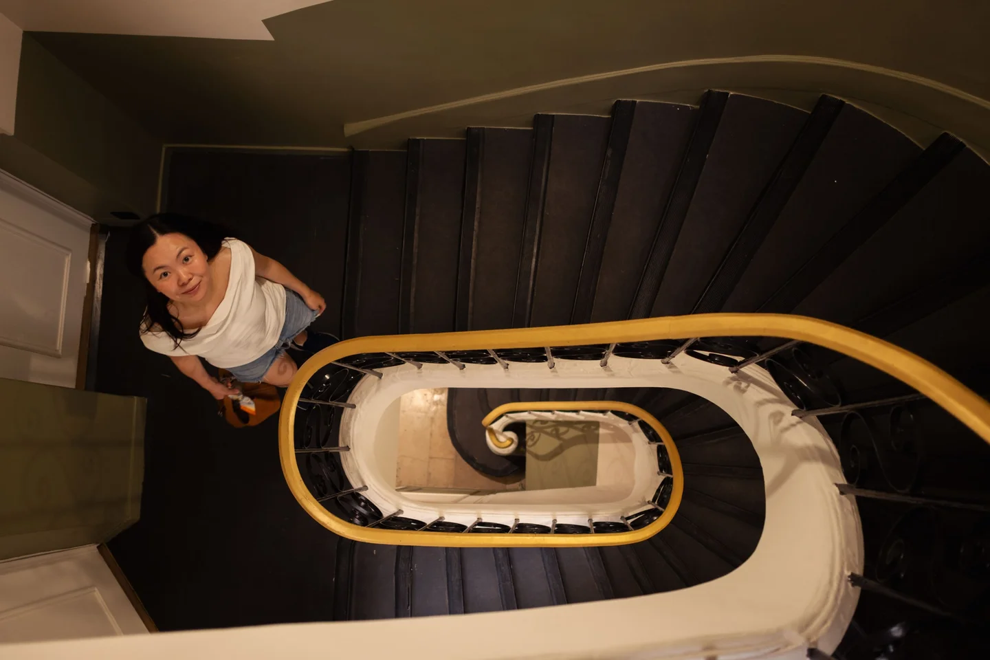 Woman looking up from a spiral staircase with a yellow handrail.