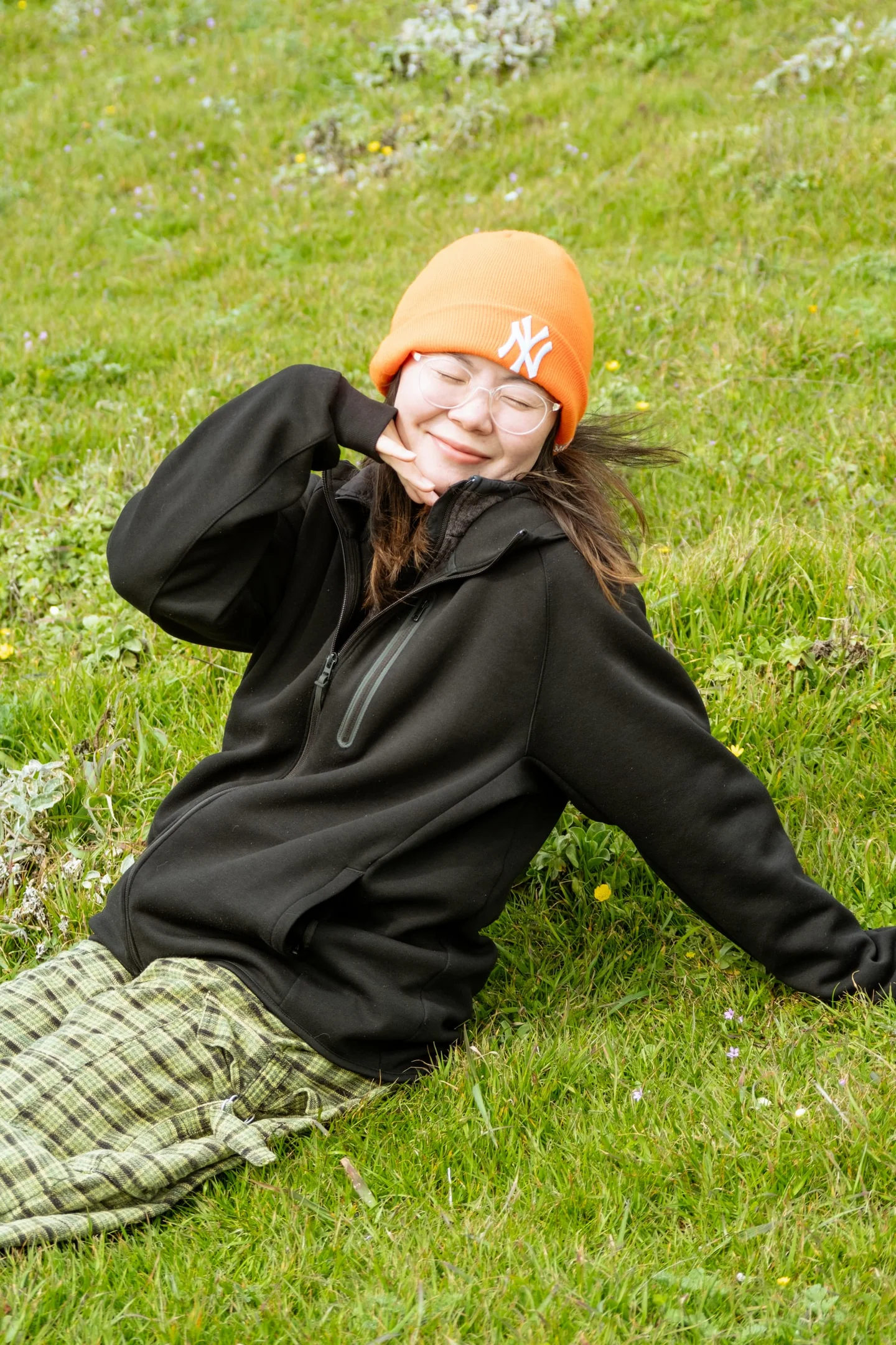 Woman in an orange knit hat reclining on green grass.