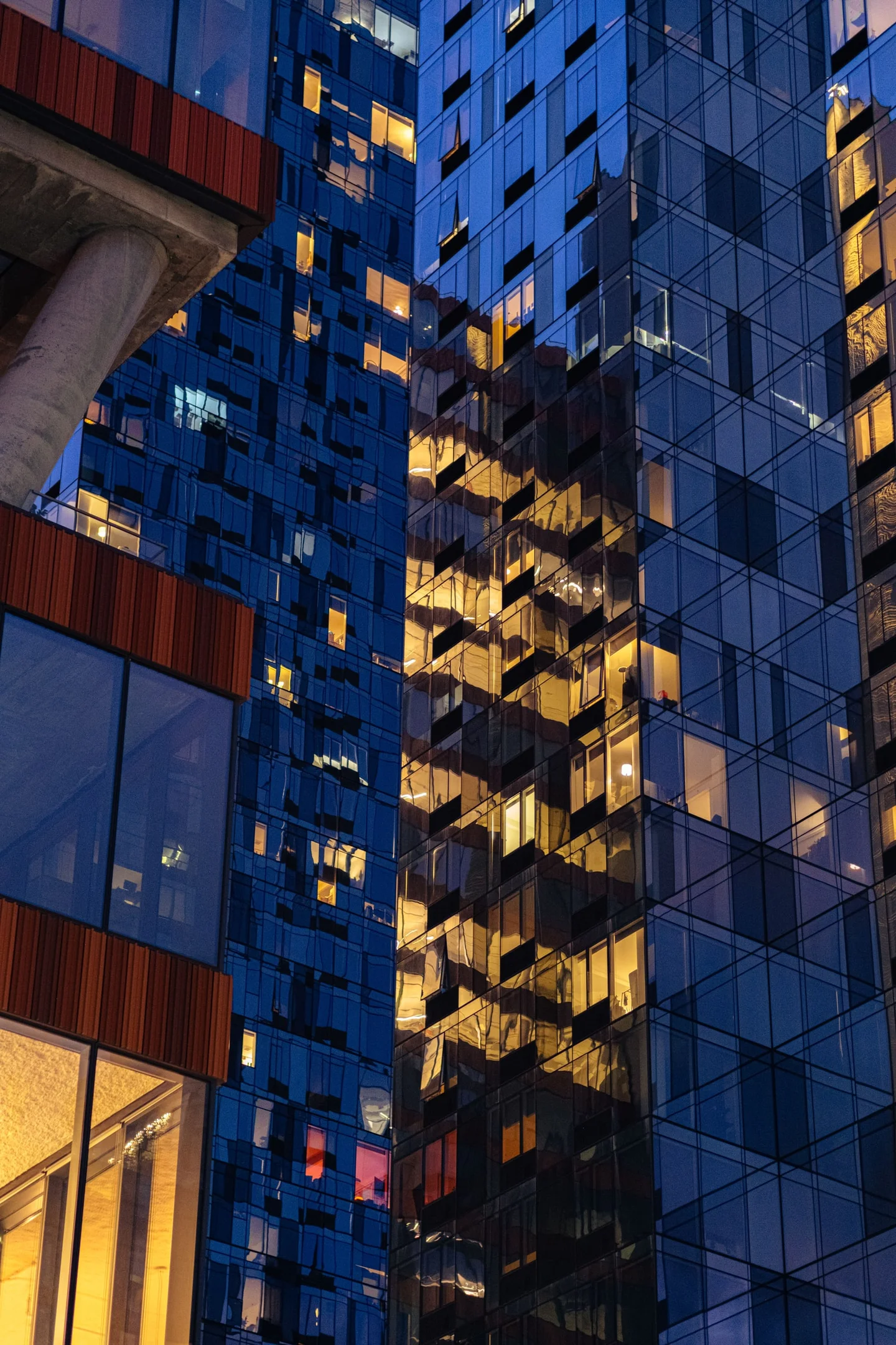 Warmly lit windows and reflections across blue glass towers at dusk.